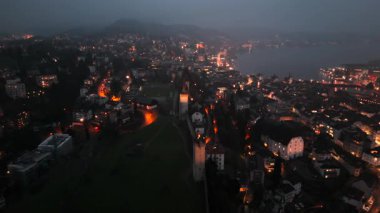 Musegg Wall ve dokuz kulesi geceleri İsviçre 'nin Lucerne kentindeki parlayan şehre bakıyor. Lucerne 'in ortaçağ savunması. Museggmauer Luzern und ihre neun Tuerme Luftaufnahme bei Nacht. 