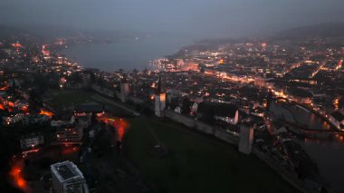 Musegg Wall ve dokuz kulesi geceleri İsviçre 'nin Lucerne kentindeki parlayan şehre bakıyor. Lucerne 'in ortaçağ savunması. Museggmauer Luzern und ihre neun Tuerme Luftaufnahme bei Nacht. 