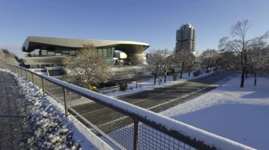 Karlı Münih, Almanya. BMW Welt, BMW Kulesi ve karargah parlak kış güneşi altında parlıyor. Modern mimari şehir zarafetiyle buluşuyor, karla kaplı sokaklar ve berrak mavi gökyüzü. Kış şehri
