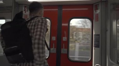 Sırt çantalı bir adam sırtı kamerayla Münih, Almanya 'da S-Bahn treninin sürgülü kapısının yanında duruyor. Şehirdeki toplu taşıma sisteminde her gün gidip gelen bir durağın çıkışını bekliyor.