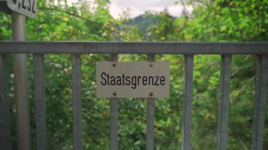 Schilder Grenze zwischen Deutschland ve Oesterreich. Tafel Staatsgrenze. Politische Grenze. Schild Grenzlinie zwischen Staatsgebieten. Çit Almanya 'da devlet sınırını işaret ediyor. Almanca Kenarlık Yazısı