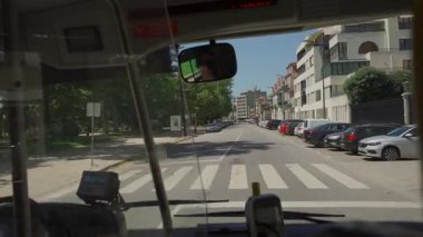 17 Ağustos 2023, Porto, Portekiz. Portekiz 'in Oporto kentindeki şehir otobüsünün ön camından güneşli yaz şehrini görüyoruz. Güneşli bir günde şehir trafiğini, yolları, arabaları ve şehir yaşamını gösteren otobüsten görüntü. 