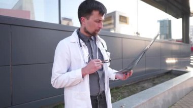Beyaz önlüklü ve gözlüklü genç bir doktor hastanenin önünde bekliyor. Tomografi çekiyor. Kısa bir sigara molası için dışarı çıktı ama molasında tıbbi görüntüler analiz edilerek çalışmaya zorlandı.. 