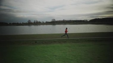 Almanya 'da parkta göl boyunca koşan bir adam. Atletik genç insan doğada koşar. Sağlıklı bir yaşam tarzı. Erkek, Münih 'teki bir şehir parkında gölet kenarında koşuyor. Göl kenarındaki patikada koşan adam.. 