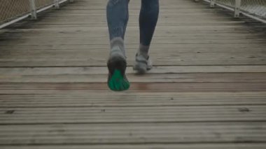 Köprü manzarasında arkadan koşan bacaklı koşucu. Erkek ayakları dışarıda, tahta yolda koşu yaparken. Dışarıdaki tahta güvertede koşan bir koşucu. Sağlıklı yaşam tarzı teması. 