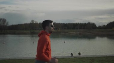 Almanya 'da parkta göl boyunca koşan bir adam. Atletik genç insan doğada koşar. Sağlıklı bir yaşam tarzı. Erkek, Münih 'teki bir şehir parkında gölet kenarında koşuyor. Göl kenarındaki patikada koşan adam.. 