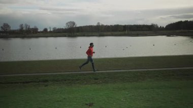 Almanya, Münih ve Almanya 'da sonbaharda parkta yürüyüş yolu boyunca koşan sporcu bir adam. Sonbaharda bir göletin yanında koşan bir erkek. Suyun yanında açık hava egzersizi. İnsanlar ve spor konsepti. 