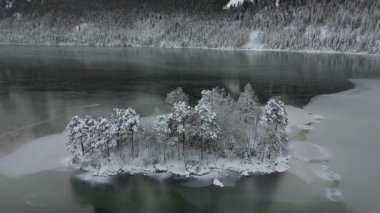 Ludwigsinsel, Heissenbuechel 'in Garmisch-Partenkirchen, Bayern, Deutschland yakınlarındaki donmuş Eibsee üzerindeki hava manzarası. Sakin kış sabahı karla kaplı ağaçları ve buz gibi gölü vurguluyor.. 