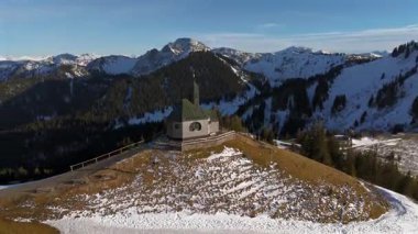 Kapelle Heilig Kreuz Rottach-Egern Tegernsee. Wallbergkapelle, Tegernsee Gölü 'ne tepeden bakan Wallberg Dağı ve güneşli bahar havasında gün batımında karla kaplı dağ sıraları. Alplerin zirvesindeki şapel. 