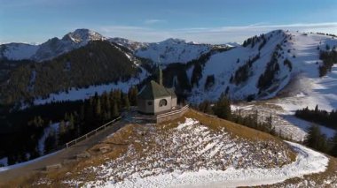 Kapelle Heilig Kreuz Rottach-Egern Tegernsee. Wallbergkapelle, Tegernsee Gölü 'ne tepeden bakan Wallberg Dağı ve güneşli bahar havasında gün batımında karla kaplı dağ sıraları. Alplerin zirvesindeki şapel. 