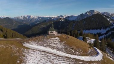 Kapelle Heilig Kreuz Rottach-Egern Tegernsee. Wallbergkapelle, Tegernsee Gölü 'ne tepeden bakan Wallberg Dağı ve güneşli bahar havasında gün batımında karla kaplı dağ sıraları. Alplerin zirvesindeki şapel. 