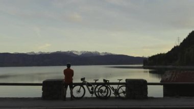 Bisikletçi arkası dönük olarak Walchensee Gölü kıyısında duruyor ve Bavyera Alpleri 'nin üzerindeki günbatımını seyrediyor. Yakınlarda iki bisiklet, suda dağ yansımaları, temiz hava, macera, özgürlük ve sükunet.. 