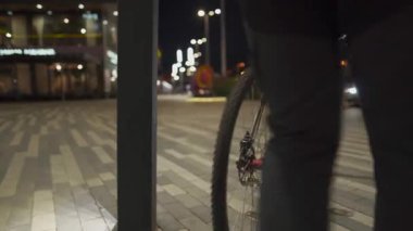 Korumalı maske takan erkek bisikletçi, bisiklet parkının dışındaki direğe şehir ışıklarının ışığında parlıyor. Bisiklet altyapısı eksikliği. Bisikleti şişir. 