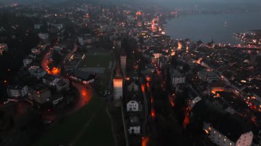 Musegg Wall ve dokuz kulesi geceleri İsviçre 'nin Lucerne kentindeki parlayan şehre bakıyor. Lucerne 'in ortaçağ savunması. Museggmauer Luzern und ihre neun Tuerme Luftaufnahme bei Nacht. 
