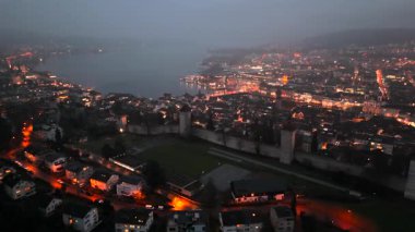 Musegg Wall ve dokuz kulesi geceleri İsviçre 'nin Lucerne kentindeki parlayan şehre bakıyor. Lucerne 'in ortaçağ savunması. Museggmauer Luzern und ihre neun Tuerme Luftaufnahme bei Nacht. 