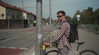 Ekose gömlek ve sırt çantası giyen bisikletçi, Almanya 'nın Münih kentindeki yaya geçidinde trafik ışıklarında Anforderungstaster' a basarak bekliyor. Kentsel hareketlilik ve bisiklet trafiği. 