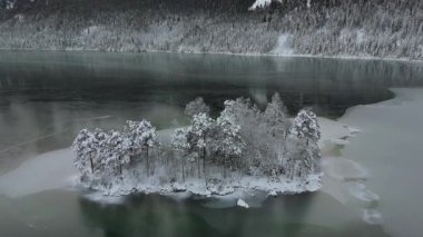 Ludwigsinsel, Heissenbuechel 'in Garmisch-Partenkirchen, Bayern, Deutschland yakınlarındaki donmuş Eibsee üzerindeki hava manzarası. Sakin kış sabahı karla kaplı ağaçları ve buz gibi gölü vurguluyor.. 