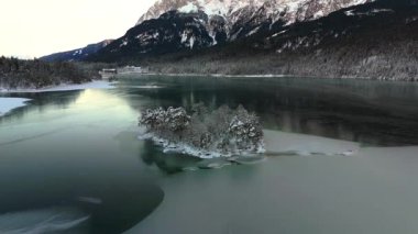 Ludwigsinsel, Heissenbuchel 'in Garmisch-Partenkirchen, Bavyera, Almanya yakınlarındaki donmuş Eibsee Gölü üzerindeki hava manzarası. Karla kaplı ağaçlar ve buzlu sularla huzurlu bir kış sabahı büyülü bir manzara yaratır.. 
