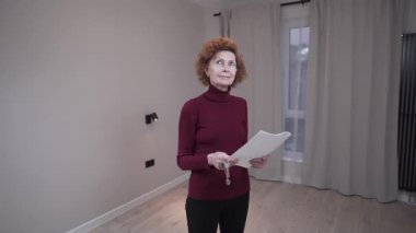 Olgun bir kadın boş küçük bir daireyi inceliyor ve elinde kira sözleşmesi tutuyor. Yaşlı kadın kira birimini denetliyor ve sözleşmeyi okuyor. Mobilyasız stüdyo daire kiralama teması. 