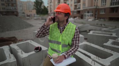 İnşaat mühendisi yüksek binalardaki beton binalarda, başlık takarak oturuyor. Yemek molasında, dışarıda dinleniyor, temiz havanın tadını çıkarıyor, kahve içiyor, telefonda konuşuyor.. 