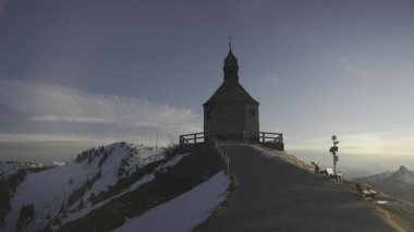 Kapelle Heilig Kreuz Rottach-Egern, Bavyera, Almanya 'da Tegernsee Gölü yakınlarında kışın gün batımında. Karlı dağ manzaraları, sakin doğa ve Bavyera dağ manzarası ile çevrili büyüleyici bir şapel.. 