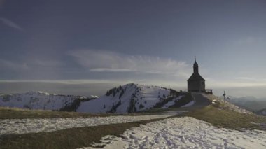 Kapelle Heilig Kreuz Rottach-Egern, Bavyera, Almanya 'da Tegernsee Gölü yakınlarında kışın gün batımında. Karlı dağ manzaraları, sakin doğa ve Bavyera dağ manzarası ile çevrili büyüleyici bir şapel.. 