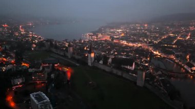 Musegg Wall ve dokuz kulesi geceleri İsviçre 'nin Lucerne kentindeki parlayan şehre bakıyor. Lucerne 'in ortaçağ savunması. Museggmauer Luzern und ihre neun Tuerme Luftaufnahme bei Nacht. 