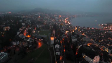 Musegg Wall ve dokuz kulesi geceleri İsviçre 'nin Lucerne kentindeki parlayan şehre bakıyor. Lucerne 'in ortaçağ savunması. Museggmauer Luzern und ihre neun Tuerme Luftaufnahme bei Nacht. 
