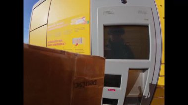 Güneşli bir günde Almanya 'da sarı DHL ambalaj dolabı kullanan bir kadını ilk gören kişi. Dişi eller dolaba bir paket yerleştiriyor ve teslimat için dokunmatik ekranı kullanıyor.. 