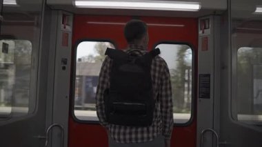 Sırt çantası ve gömlek giyen adam Almanya 'nın Münih şehrinde S-Bahn treninin sürgülü kapısının yanında duruyor. Durağının inmesini bekliyor. Şehir toplu taşıma ağındaki günlük seyahatini resmediyor.. 