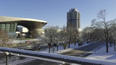 Karlı Münih, Almanya. BMW Welt, BMW Kulesi ve karargah parlak kış güneşi altında parlıyor. Modern mimari şehir zarafetiyle buluşuyor, karla kaplı sokaklar ve berrak mavi gökyüzü. Kış şehri