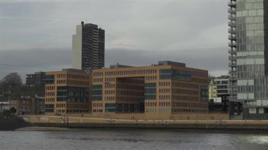 Almanya 'nın Hamburg limanındaki modern binalar. Bulutlu bir gökyüzünün altında nehir manzaralı şehir mimarisi. Modern Avrupa şehir yaşamını yansıtan çağdaş şehir manzarası. Hamburg, Almanya. 