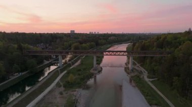 Grosshesselohe Köprüsü, Isar Kanalı, bisiklet yolu ve yemyeşil doğayı gösteren, Isar Vadisi üzerinde gün batımı drone çekimi. Münih 'te romantik bir akşam ışığı. Hava manzarası, Almanya. luftaufnahme Grosshesseloher Brucke