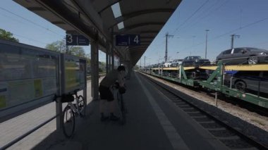 Bisikletçi, Münih Trudering İstasyonu 'ndaki platformda, iki katlı bir vagon taşıyıcı tren tamamen karşı tarafta araçlarla dolu duruyor. Tren, verimli demiryolu temelli taşıma sisteminin bir parçasıdır.