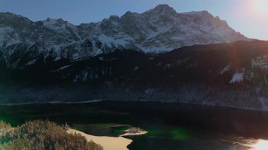 Eibsee Gölü 'nün ve Almanya' nın Bavyera kentindeki Zugspitze dağının insansız hava aracı görüntüsü. Karla kaplı Alpler, kristal berrak su, orman ve güneş ışığıyla manzaralı bir kış manzarası. Mükemmel seyahat hedefi. 