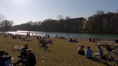 27 Nisan 2022. Münih, Almanya. Sonniger Fruehlingstag im Zentrum Muenchens: Ben Isarufer bei der Kirche St. Maximilian entspannen sich Menschen, geniessen die Sonne und die urbane Natur. 