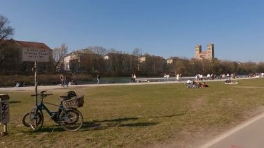 Sonniger Fruehlingstag im Zentrum Muenchens: Ben Isarufer bei der Kirche St. Maximilian entspannen sich Menschen, geniessen die Sonne und die urbane Natur. 