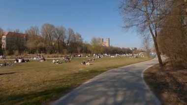 27 Nisan 2022. Münih, Almanya. Münih 'in merkezinde güneşli bir bahar günü. Yerel halk ve turistler, dinlenmek, güneşlenmek ve kentsel doğanın tadını çıkarmak için St. Maximilian Kilisesi yakınlarındaki Isar nehri kıyısında toplandılar.. 