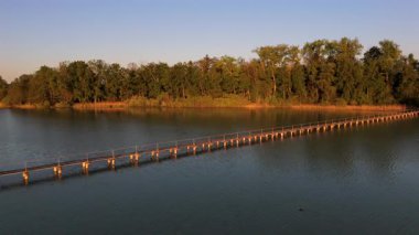 Luftaufnahme der 260 m langen befahrbaren Holzbruecke zur Mausinsel im Woerthsee, Bayern. Öl er Insel ist dicht bewaldet und liegt ruhig im Landschaftsschutzgebiet bei Inning am Ammersee. 