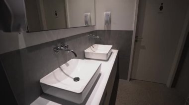 Çağdaş kadın tuvaletinin içinde çift lavabo, büyük bir ayna, sabunluklar ve kadın imzalı bir giriş kapısı var. Temiz, hijyenik ve minimalist umumi tuvalet tasarımı. 