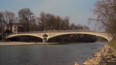 Münih, Almanya. Münih 'in tarihi merkezinde bahar günü Mariannenbruecke ve St. Lukas Kilisesi yakınlarındaki Isar Nehri boyunca berrak mavi gökyüzü altında gezinen yerliler. 