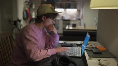 Evde dizüstü bilgisayarda çalışan Freelancer. Şapkalı ve pembe kazaklı bir kadın geceleri küçük bir dairede defterinin başında çalışıyor. Kadın, son teslim tarihine odaklanmış, küçük dairesinden uzaktan çalışıyor.. 