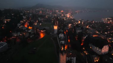 Musegg Wall ve dokuz kulesi geceleri İsviçre 'nin Lucerne kentindeki parlayan şehre bakıyor. Lucerne 'in ortaçağ savunması. Museggmauer Luzern und ihre neun Tuerme Luftaufnahme bei Nacht. 