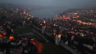 Musegg Wall ve dokuz kulesi geceleri İsviçre 'nin Lucerne kentindeki parlayan şehre bakıyor. Lucerne 'in ortaçağ savunması. Museggmauer Luzern und ihre neun Tuerme Luftaufnahme bei Nacht. 