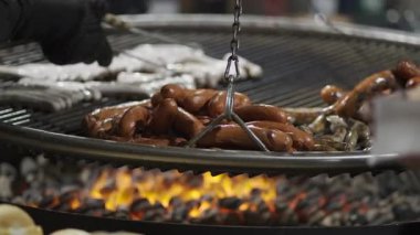 Şeflerin elleri kışın Almanya 'da Noel pazarında ateşte asılı duran metal ızgarada sosis pişiriyor. Akşamları Noel Fuarı 'nda farklı türde sosisli barbekü. Bayerische Wurste. 