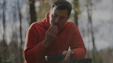 Bir adam, bir turist, sonbahar ormanlarında yürüyüş yaparken öğle yemeği arasında sandviç yemekten hoşlanır. Ağaç kütüğünün yanında otururken, portatif tencere ve çatal bıçak kullanır, güneşli açık hava yemeğini takdir eder.. 