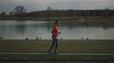 Almanya, Münih ve Almanya 'da sonbaharda parkta yürüyüş yolu boyunca koşan sporcu bir adam. Sonbaharda bir göletin yanında koşan bir erkek. Suyun yanında açık hava egzersizi. İnsanlar ve spor konsepti. 