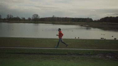 Almanya 'da parkta göl boyunca koşan bir adam. Atletik genç insan doğada koşar. Sağlıklı bir yaşam tarzı. Erkek, Münih 'teki bir şehir parkında gölet kenarında koşuyor. Göl kenarındaki patikada koşan adam.. 
