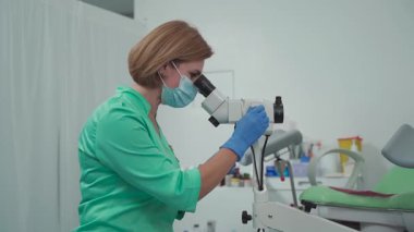 Gynecologist uses colposcope. Optical device with magnification designed for detailed examination of cervix, vagina, and vulva, aiding in diagnosing pathologies and detecting precancerous changes. 