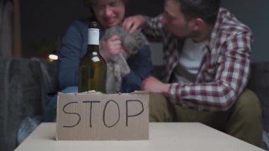 Psikolojik ve fiziksel istismarı gösteren aile içi çatışma sahnesi. Sıkıntılı bir kadın, kedi yavrusunu saldırgan bir erkekten korur. Aile içi şiddeti ve alkolle ilgili saldırganlığı simgeler.